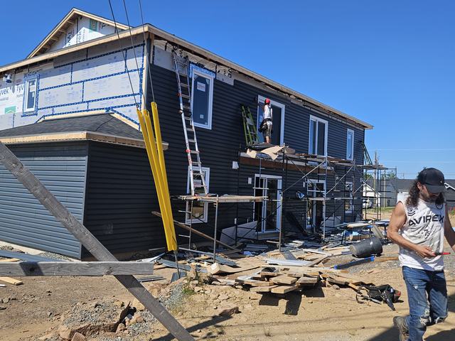 Workers installing dark vinyl siding on a two-storey residential home under construction with scaffolding in place.