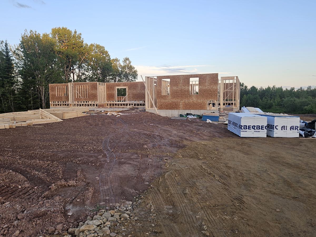 Brick residential home in early framing stage with wood walls and roof structure under construction.
