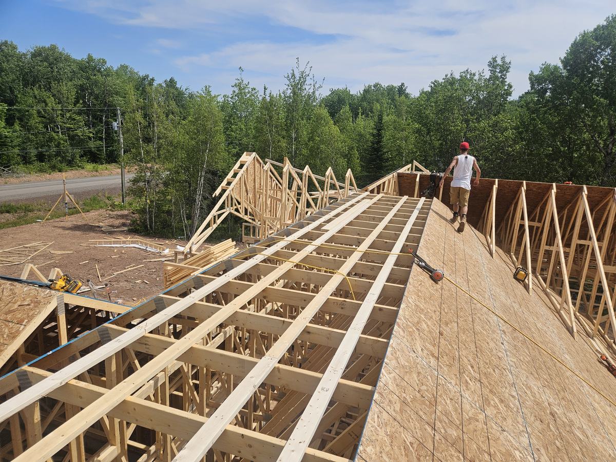 Workers installing roof trusses and sheathing on a residential home under construction.