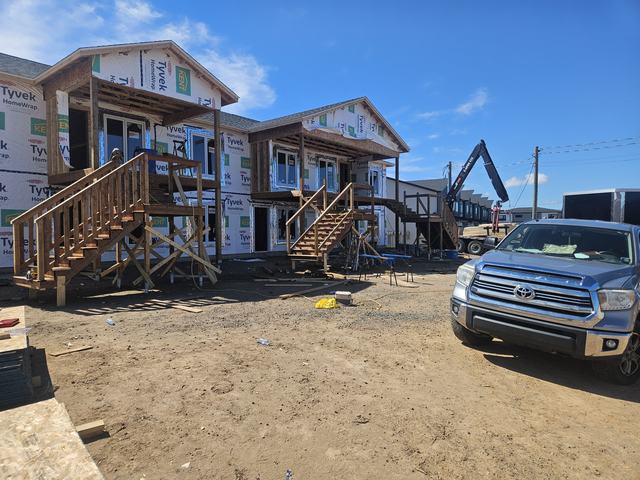 Two-storey homes in framing stage with Tyvek house wrap and wooden stairs installed on sandy lot.