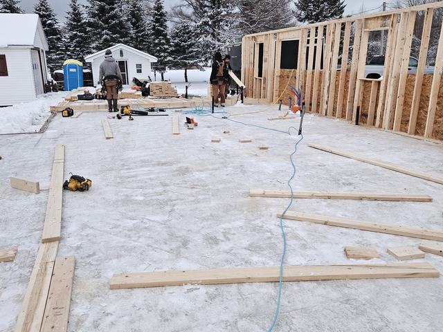 Wooden framing walls under construction on a residential home foundation in winter conditions.