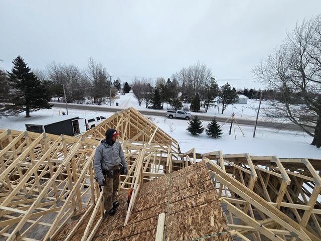 Worker on roof trusses during framing stage of a residential home construction project.