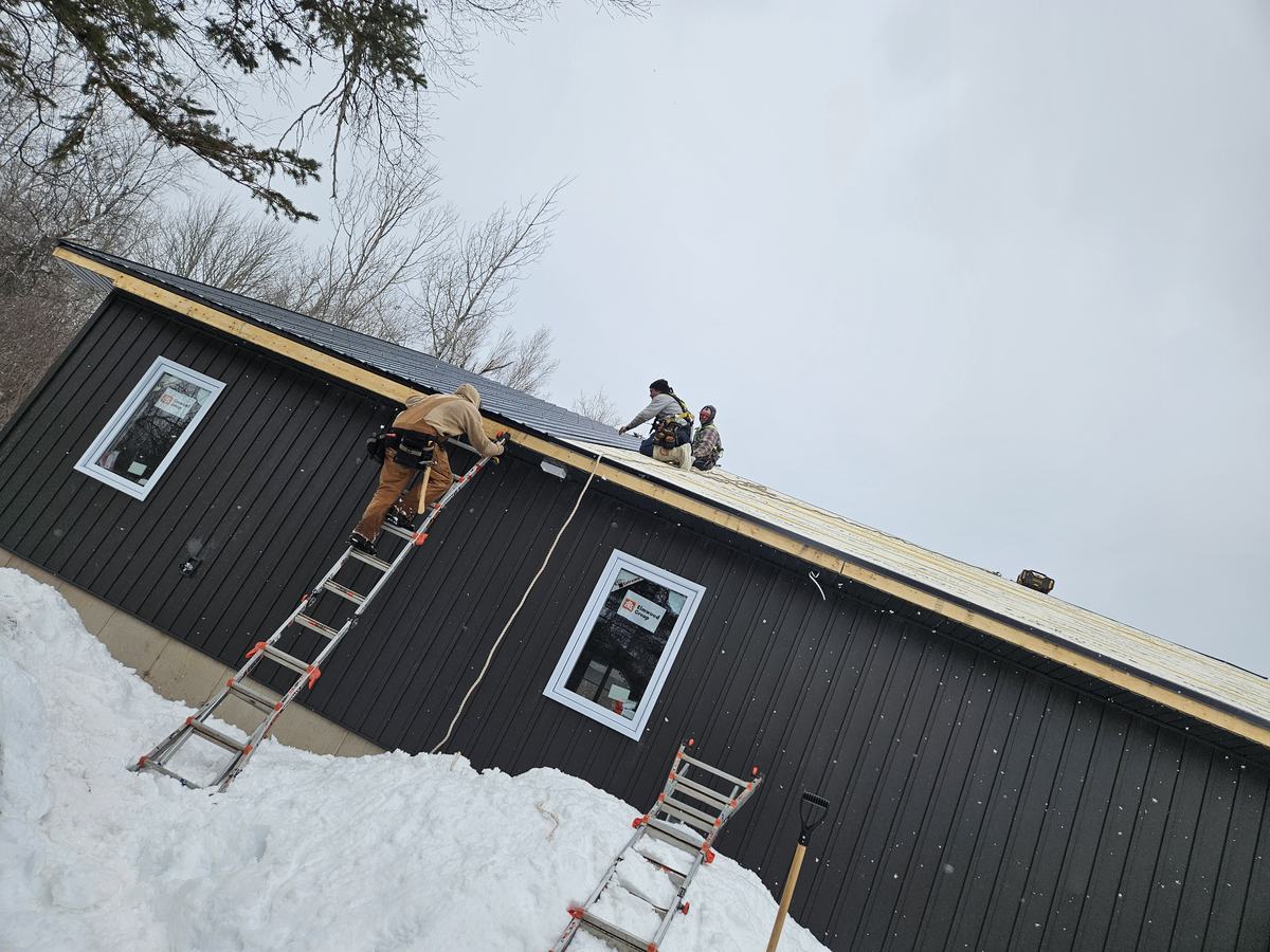 Workers installing metal roof panels on a single story home during winter construction.