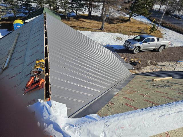 Metal roof sheeting being installed on a residential structure with underlayment and sheathing visible.
